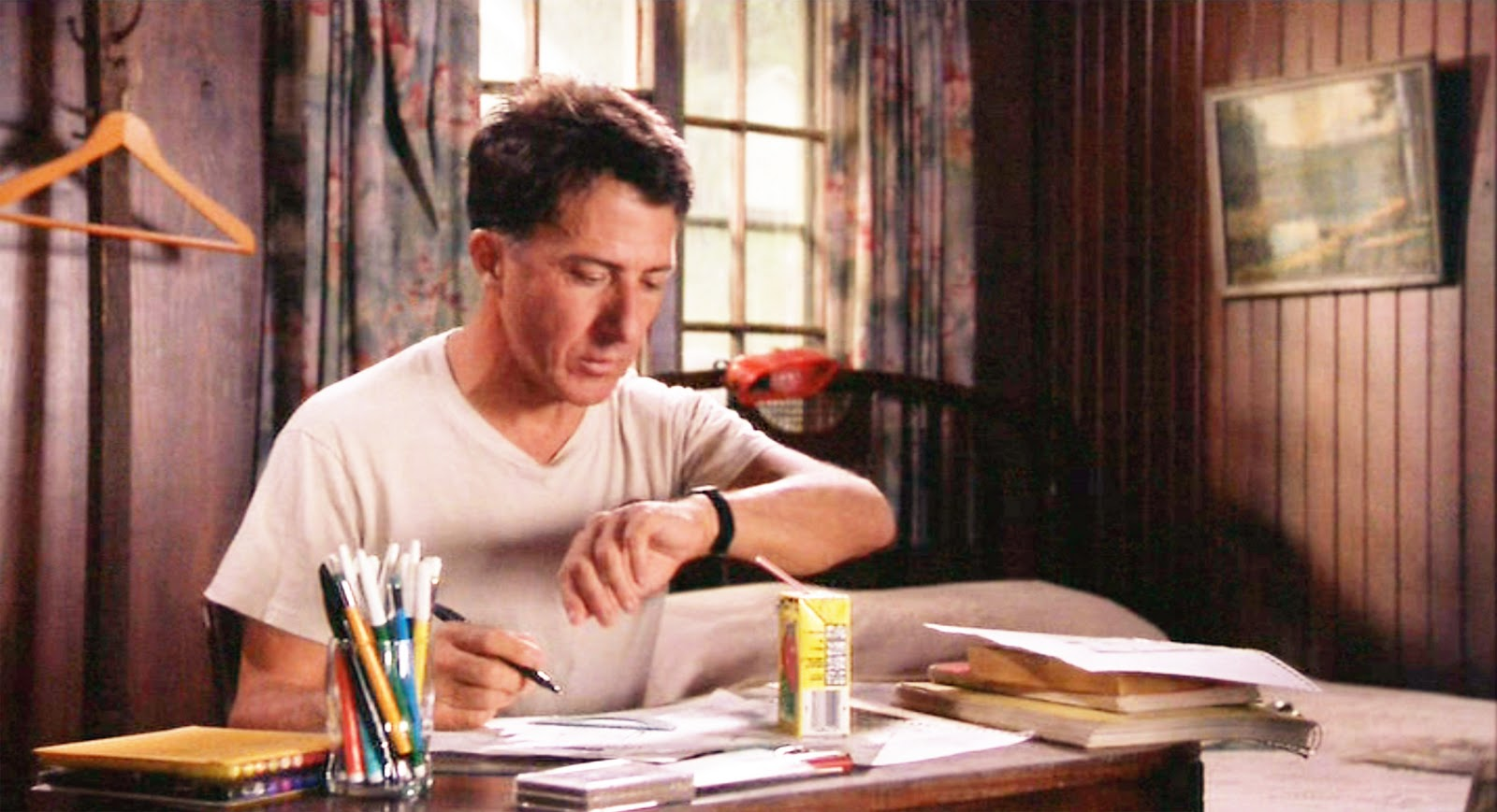 How Pop Culture Defines Autism Stereotypes? Dustin Hoffman as autistic character Raymond Babbitt in a scene from the 1988 film “Rain Man,” sitting at a desk with papers, pens, and a juice box, looking at his watch.